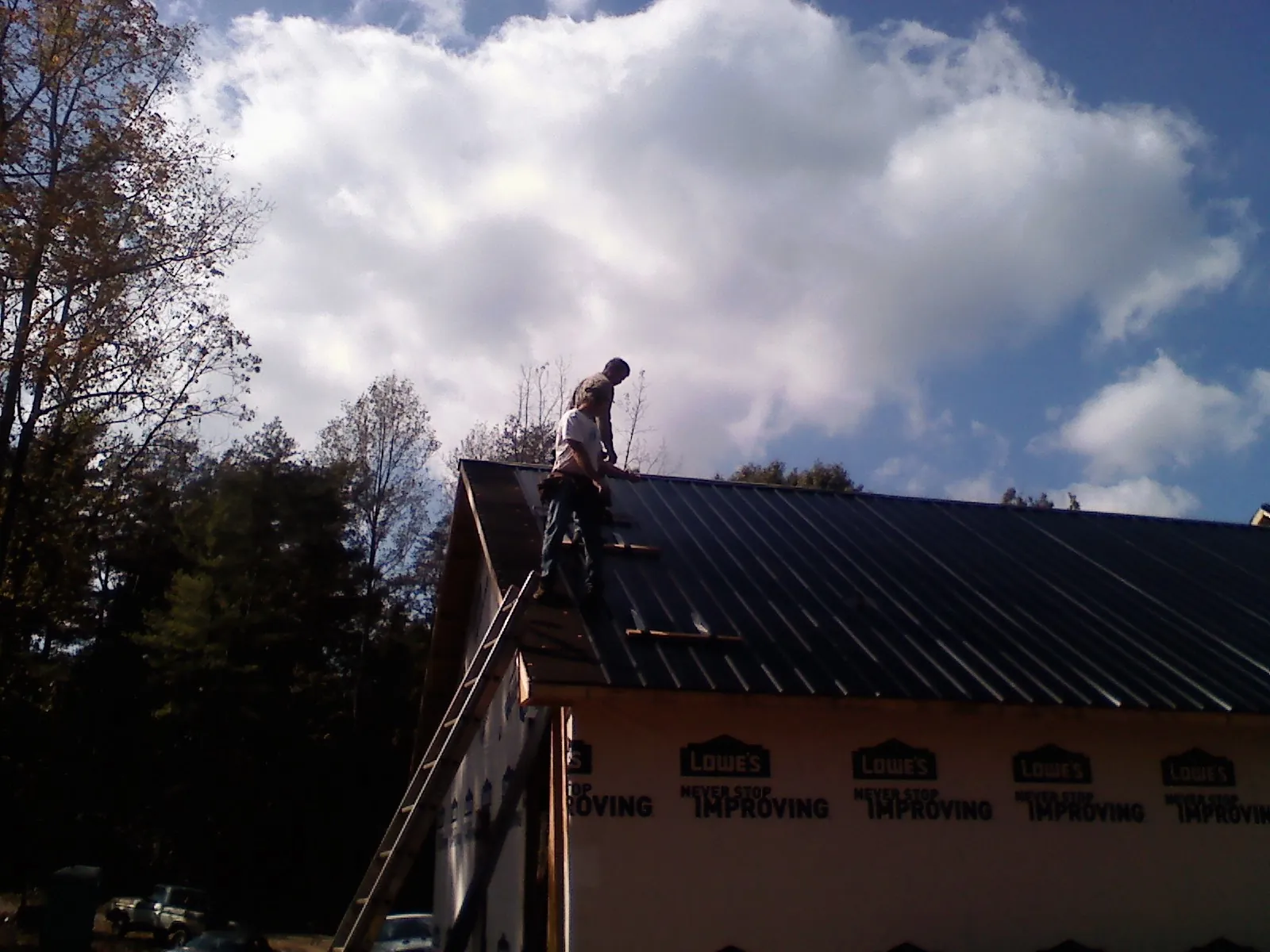 Roofer fastening dark metal panels high against a cloudy sky in Hopewell